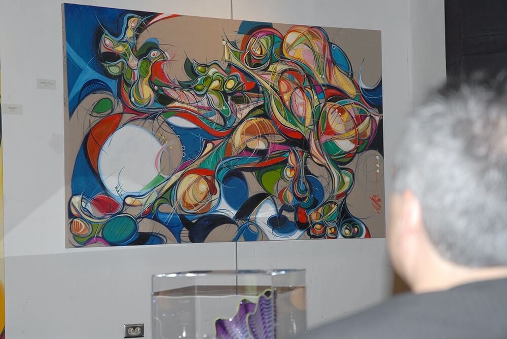 Photo of a figurative oil on linen painting by artist Michael J. Korber on the gallery wall with glass works by Chihuly the foreground at Obra Galería Alegría - Modern & Contemporary Art Gallery - Old San Juan, Puerto Rico.